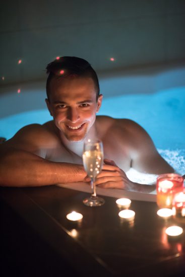 young handsome man enjoys relaxing in the jacuzzi with candles and champagne at luxury resort spa